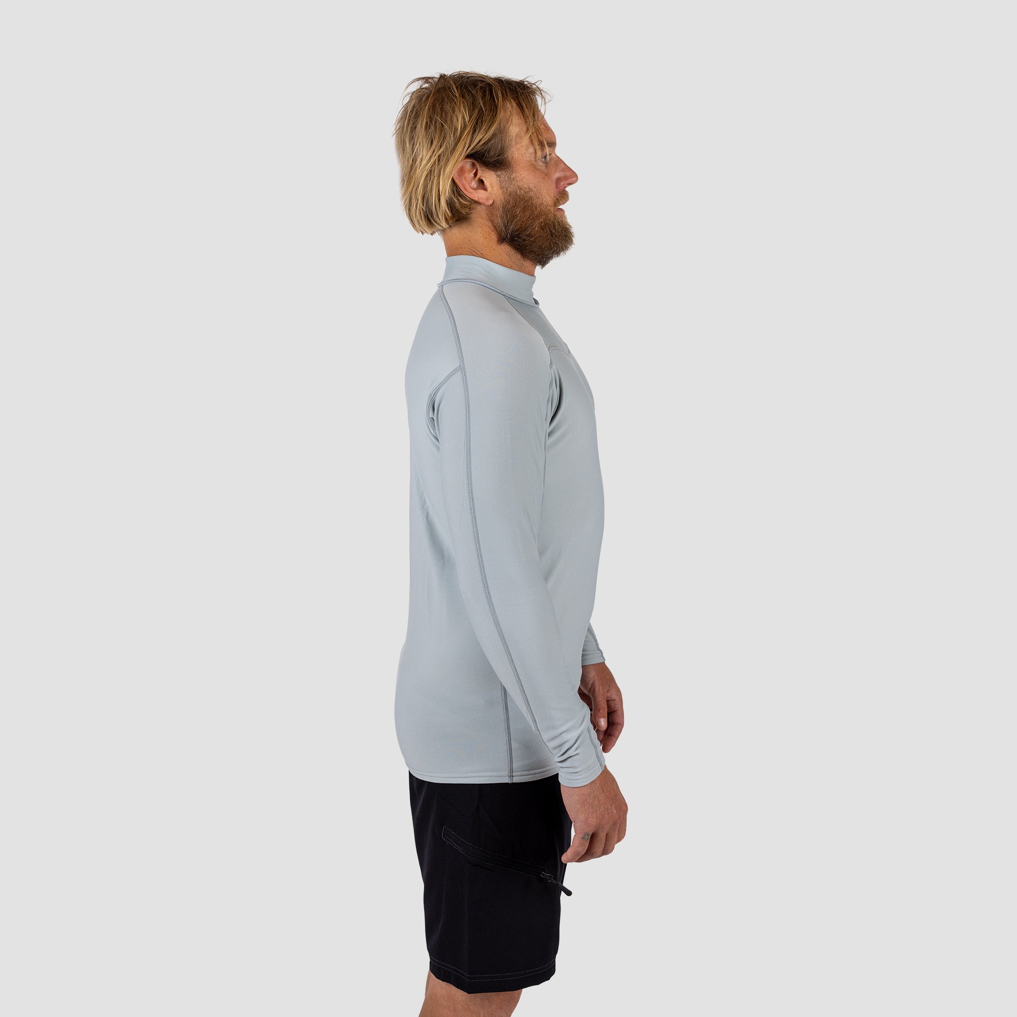 Man wearing a light gray long-sleeve Rash vest and black shark eyes instinct boardshorts on a light grey background