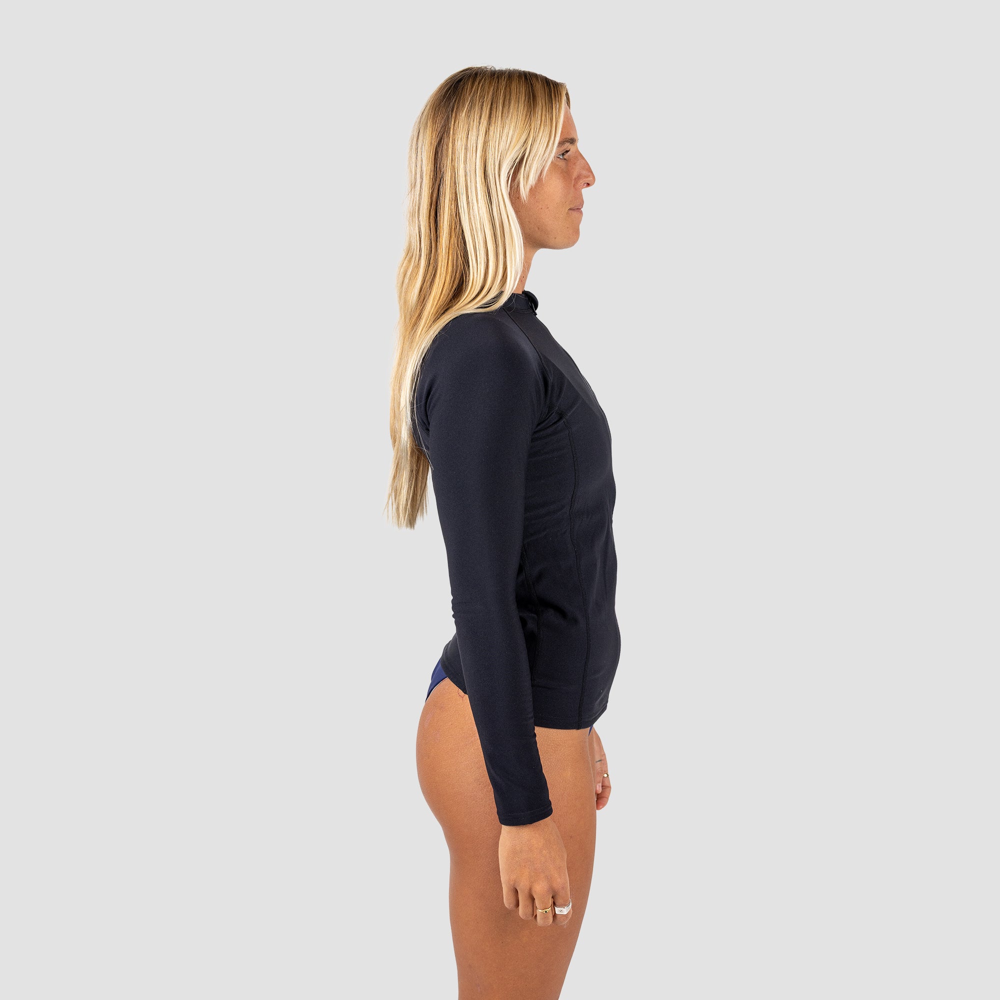 Woman wearing a black front zip long-sleeve rash vest on a gray background