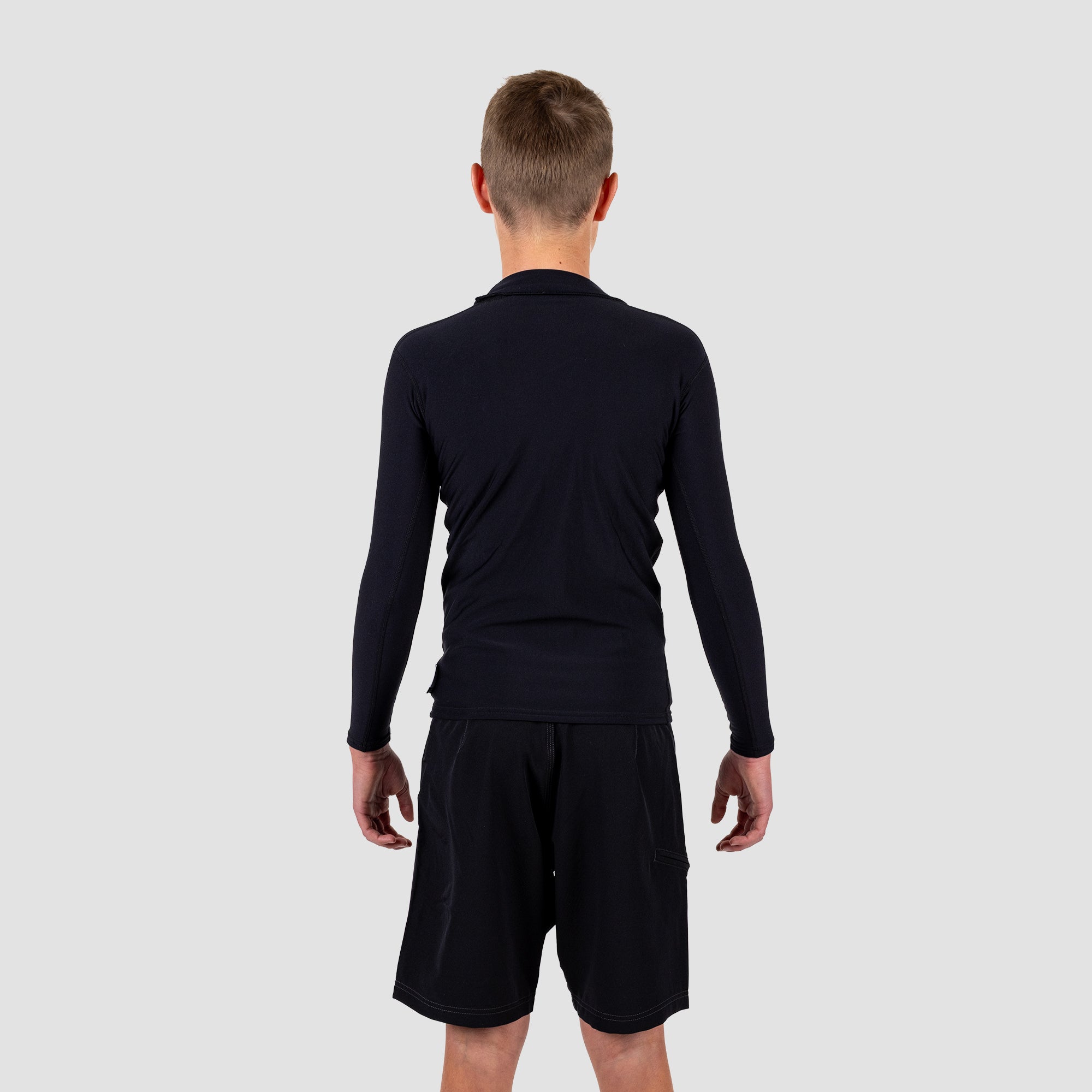 Boy wearing a black long-sleeve rash rest and shorts on a light gray background