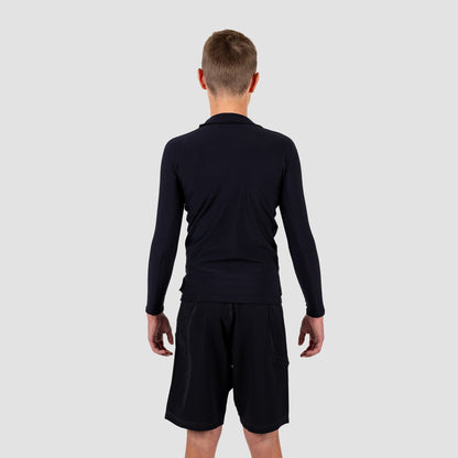 Boy wearing a black long-sleeve rash rest and shorts on a light gray background