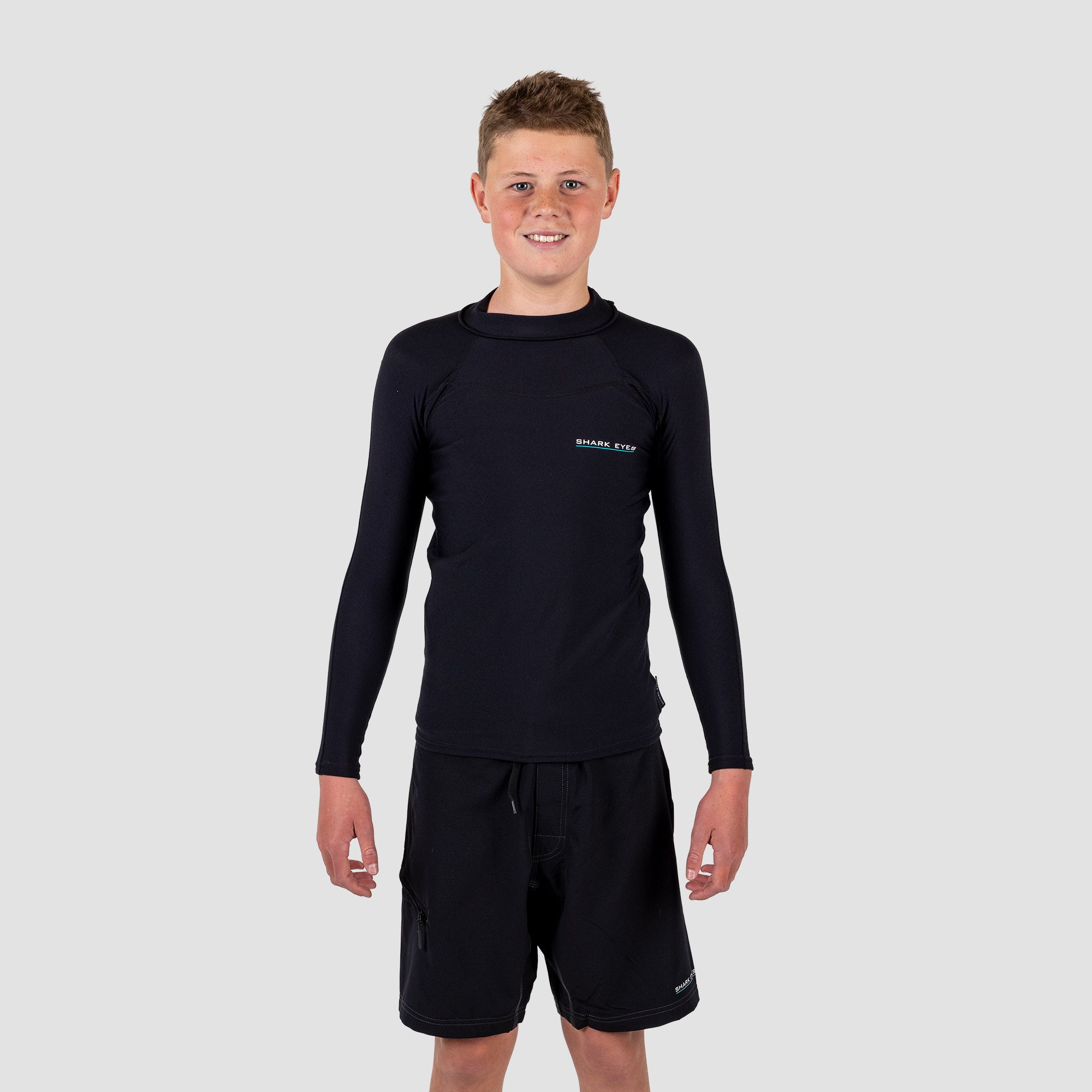 Boy wearing a black long-sleeve rash rest and shorts on a light gray background
