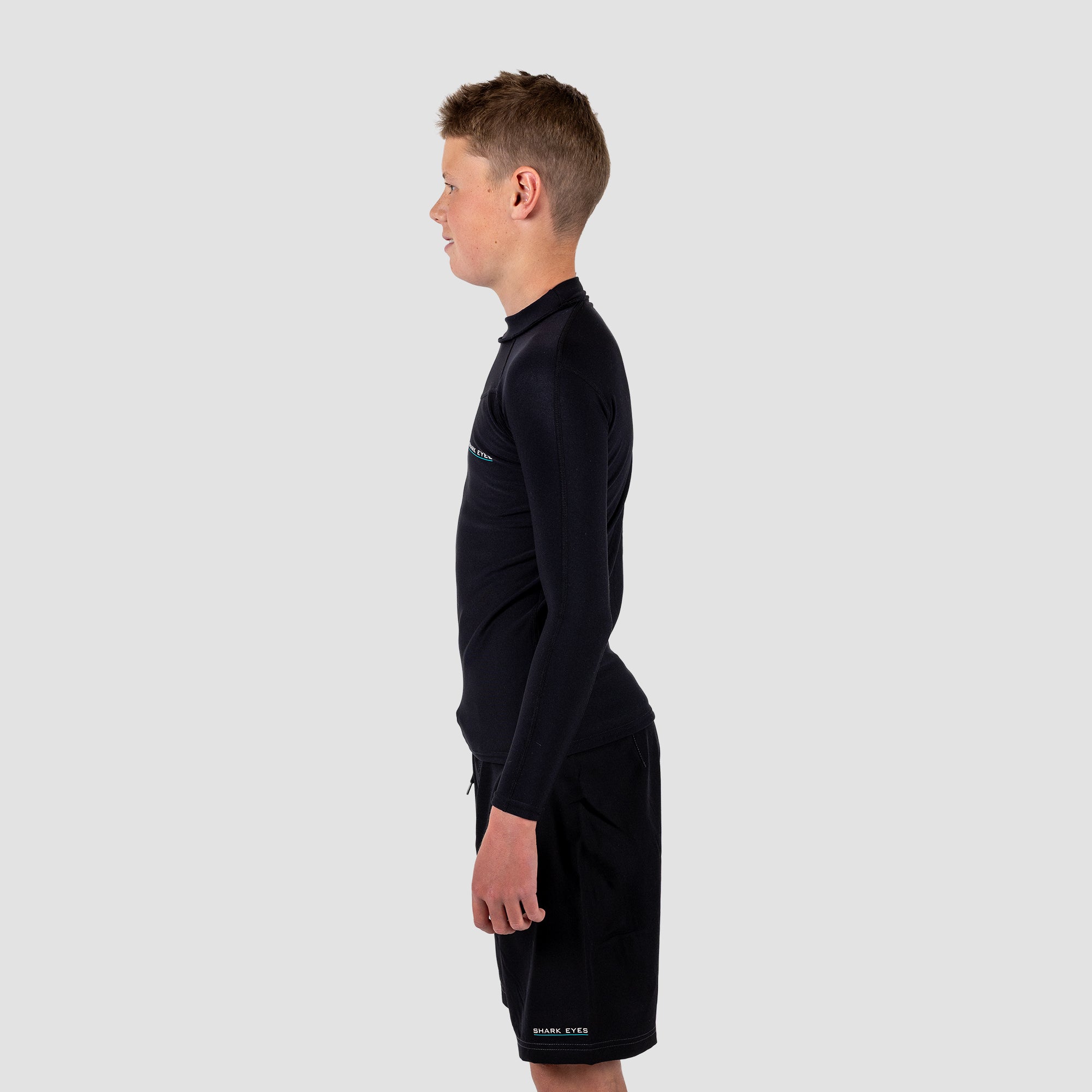 Boy wearing a black long-sleeve rash rest and shorts on a light gray background