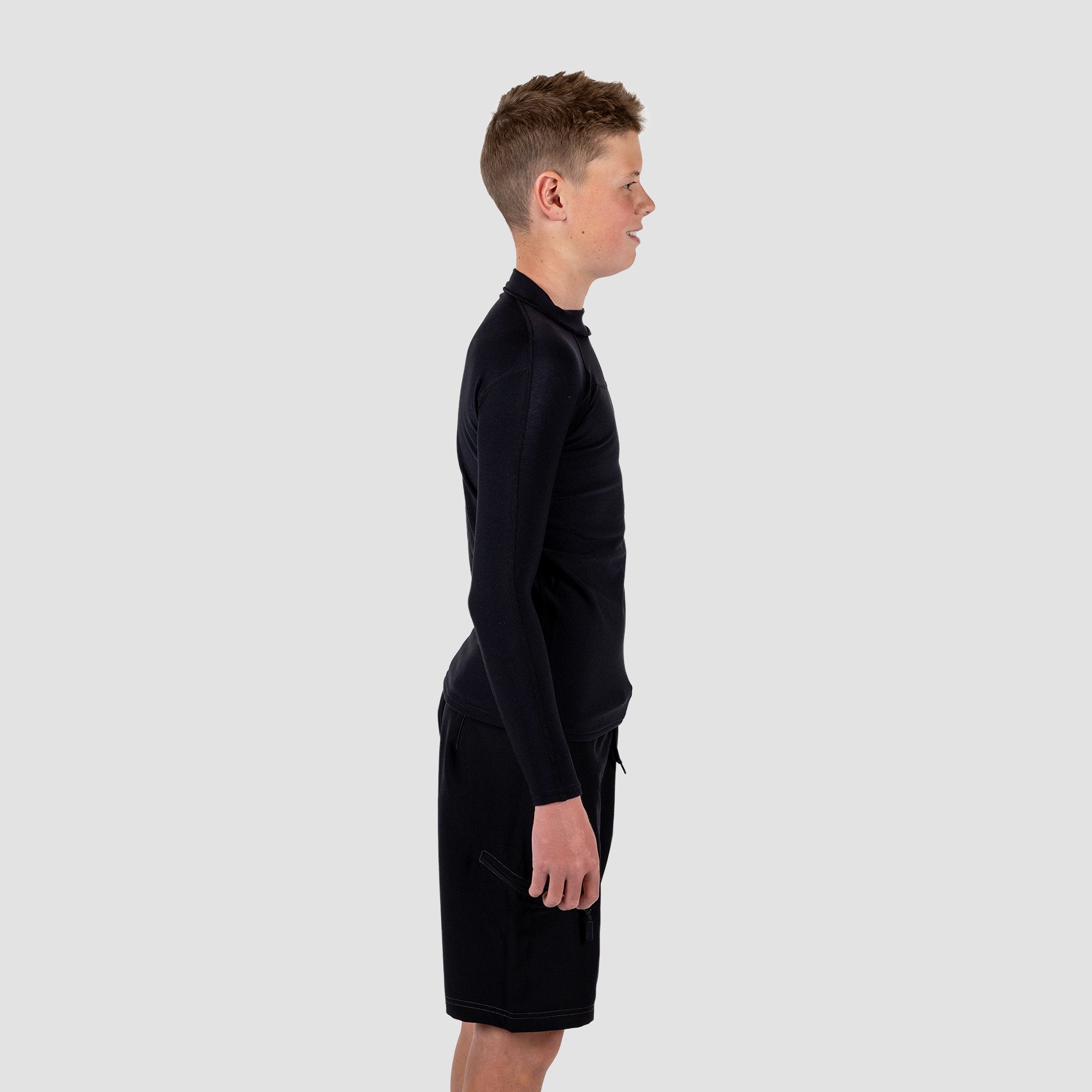 Boy wearing a black long-sleeve rash rest and shorts on a light gray background